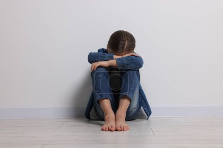 Child abuse. Upset girl sitting on floor near white wall
