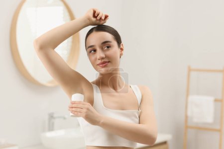Photo for Beautiful young woman applying deodorant in bathroom - Royalty Free Image