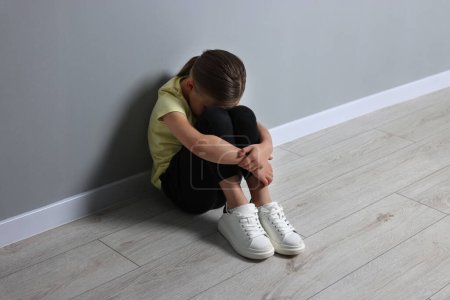Abuso infantil. Chica molesta sentada en el suelo cerca de la pared gris