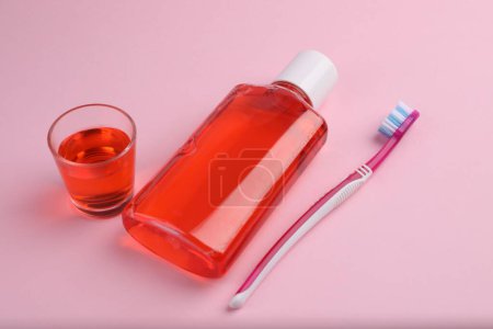 Foto de Enjuague bucal fresco en botella, vidrio y cepillo de dientes sobre fondo rosa, primer plano - Imagen libre de derechos