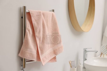Heated rail with pink towel on white wall in bathroom