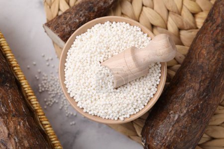 Téléchargez les photos : Perles de tapioca dans un bol et racines de manioc sur table blanche, plat - en image libre de droit