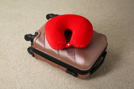 Red travel pillow and suitcase on beige rug