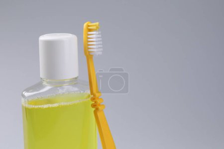 Foto de Enjuague bucal fresco en botella y cepillo de dientes sobre fondo gris, primer plano. Espacio para texto - Imagen libre de derechos