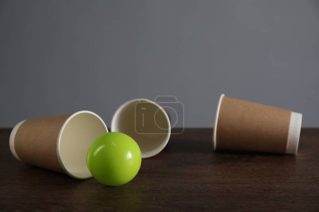 Shell game. Three paper cups and ball on wooden table