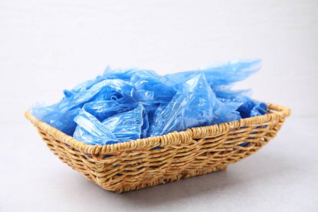 Blue medical shoe covers in wicker basket on light background, closeup