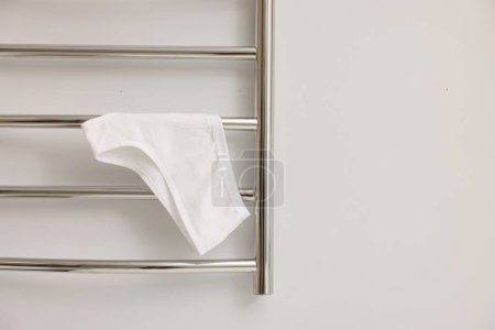 Heated towel rail with underwear on white wall, closeup. Space for text