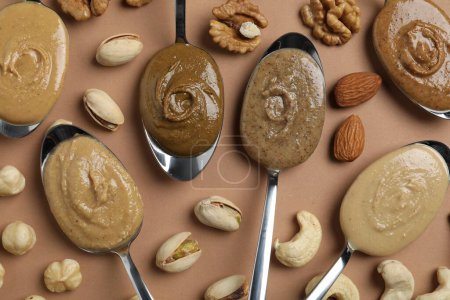 Photo for Tasty nut butters in spoons and raw nuts on light brown table, flat lay - Royalty Free Image
