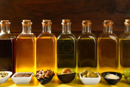 Foto de Grasas vegetales. Diferentes aceites en botellas de vidrio e ingredientes en la mesa amarilla, primer plano - Imagen libre de derechos