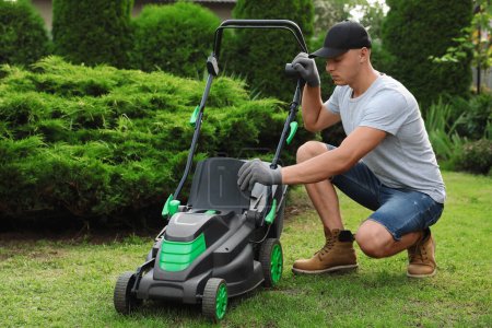 Cleaning lawn mower. Young man detaching grass catcher from device in garden