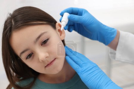 Doctor applying medical drops into girl's ear indoors