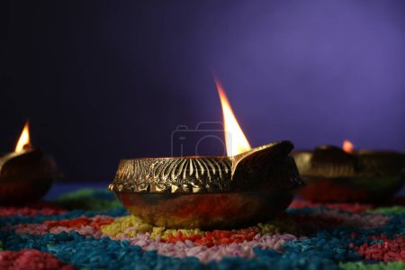 Diwali-Feier. Diya-Lampen und bunte Rangoli auf einem Tisch vor violettem Hintergrund, Nahaufnahme