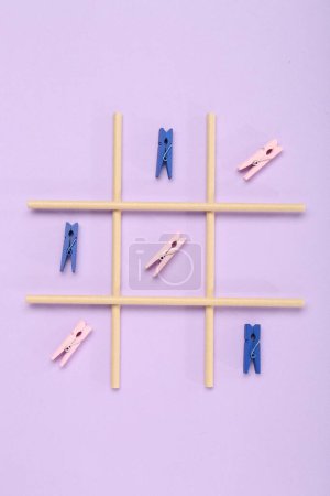 Tic tac toe game made with clothespins on lilac background, top view