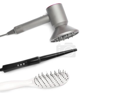 Hair dryer, curling iron and brush on white background, top view