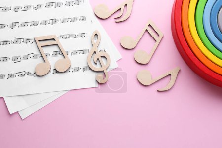 Babylieder. Notenblätter, Holznotizen und Spielzeugregenbogen auf rosa Hintergrund, flache Lage