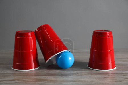 Téléchargez les photos : Jeu de coquille. Trois tasses rouges et boule sur table en bois - en image libre de droit