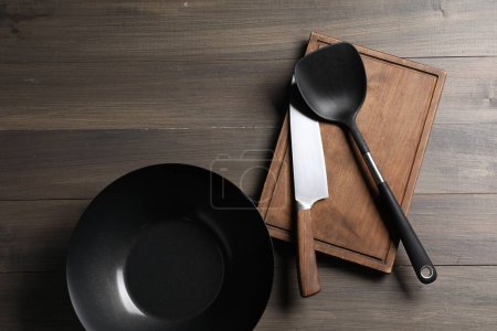 Photo for Black metal wok, knife, board and spatula on wooden table, top view - Royalty Free Image