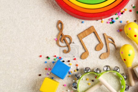 Concepto de canción de bebé. Notas de madera, instrumentos musicales para niños y juguetes en alfombra beige, puesta plana. Espacio para texto