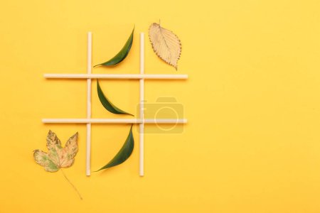 Tic tac toe game made with fresh and dry leaves on yellow background, top view. Space for text