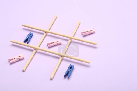 Tic tac toe game made with clothespins on violet background, space for text