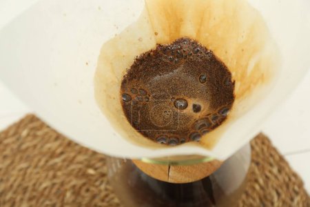 Paper filter with aromatic drip coffee in glass chemex coffeemaker on table, closeup