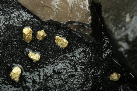 Photo for Shiny gold nuggets on wet stones, top view - Royalty Free Image