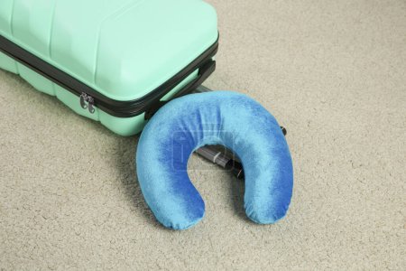 Light blue travel pillow and suitcase on beige rug