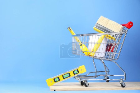 Foto de Pequeño carrito de compras con pintura y equipo de renovación sobre fondo azul claro - Imagen libre de derechos
