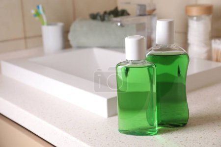 Enjuagues bucales frescos en botellas en la encimera en el baño, primer plano. Espacio para texto