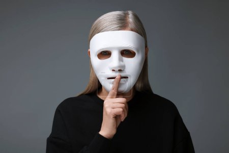 Multiples Persönlichkeitskonzept. Frau in Maske zeigt Schweigegegeste auf grauem Hintergrund
