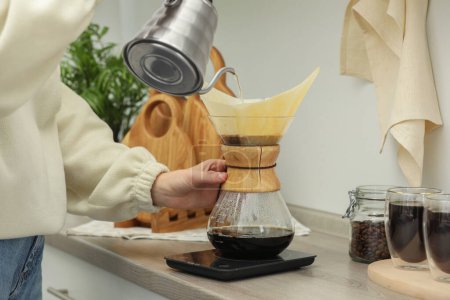 Foto de Mujer vertiendo agua caliente en la cafetera chemex vidrio con filtro de papel y café en la encimera en la cocina, primer plano - Imagen libre de derechos