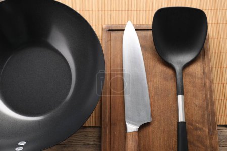 Black metal wok, knife and spatula on wooden table, top view