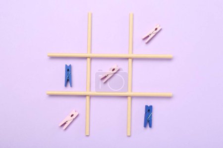 Tic tac toe game made with clothespins on violet background, top view