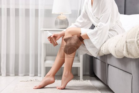 Foto de Auto-bronceado. Mujer que aplica el producto cosmético en la pierna con el guante de bronceado en la cama en casa, primer plano. Espacio para texto - Imagen libre de derechos