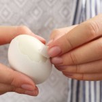 Woman peeling fresh boiled egg, closeup view