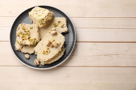 Morceaux de halva savoureux avec pistaches sur table en bois, vue sur le dessus. Espace pour le texte