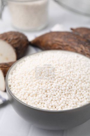 Téléchargez les photos : Perles de tapioca dans un bol et racines de manioc sur table carrelée blanche, gros plan - en image libre de droit