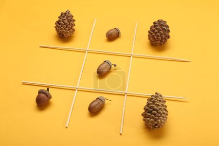 Tic tac toe game made with acorns and pine cones on yellow background