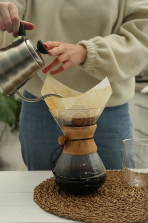 Foto de Mujer vertiendo agua caliente en la cafetera chemex vidrio con filtro de papel y café en la mesa, primer plano - Imagen libre de derechos
