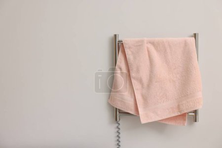 Heated rail with pink towel on white wall, space for text
