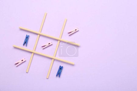 Tic tac toe game made with clothespins on violet background, top view. Space for text