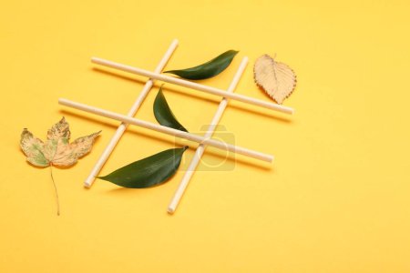 Tic tac toe game made with fresh and dry leaves on yellow background, space for text