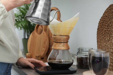 Téléchargez les photos : Femme versant de l'eau chaude dans une cafetière chemex en verre avec filtre en papier et café au comptoir dans la cuisine, gros plan - en image libre de droit