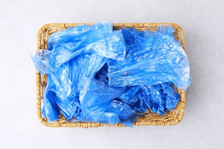 Blue medical shoe covers in wicker basket on light background, top view