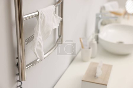 Heated towel rail with underwear on white wall in bathroom, closeup