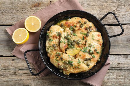 Delicious chicken piccata with herbs and lemon on wooden table, flat lay