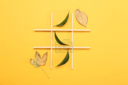 Tic tac toe game made with fresh and dry leaves on yellow background, top view