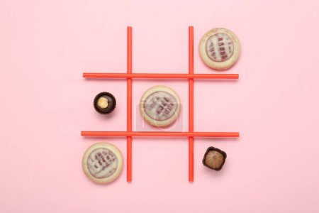 Tic Tac Toe Spiel mit Keksen und Süßigkeiten auf rosa Hintergrund, Ansicht von oben