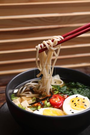 Eating delicious vegetarian ramen with chopsticks at table, closeup. Noodle soup