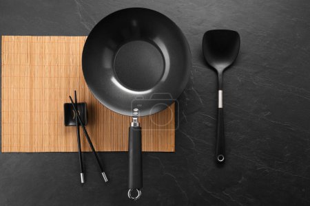 Photo for Black metal wok, chopsticks and spatula on dark textured table, top view - Royalty Free Image
